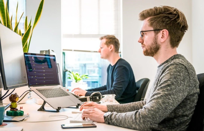 Two people working side by side on computers implementing AI for contact center solutions.